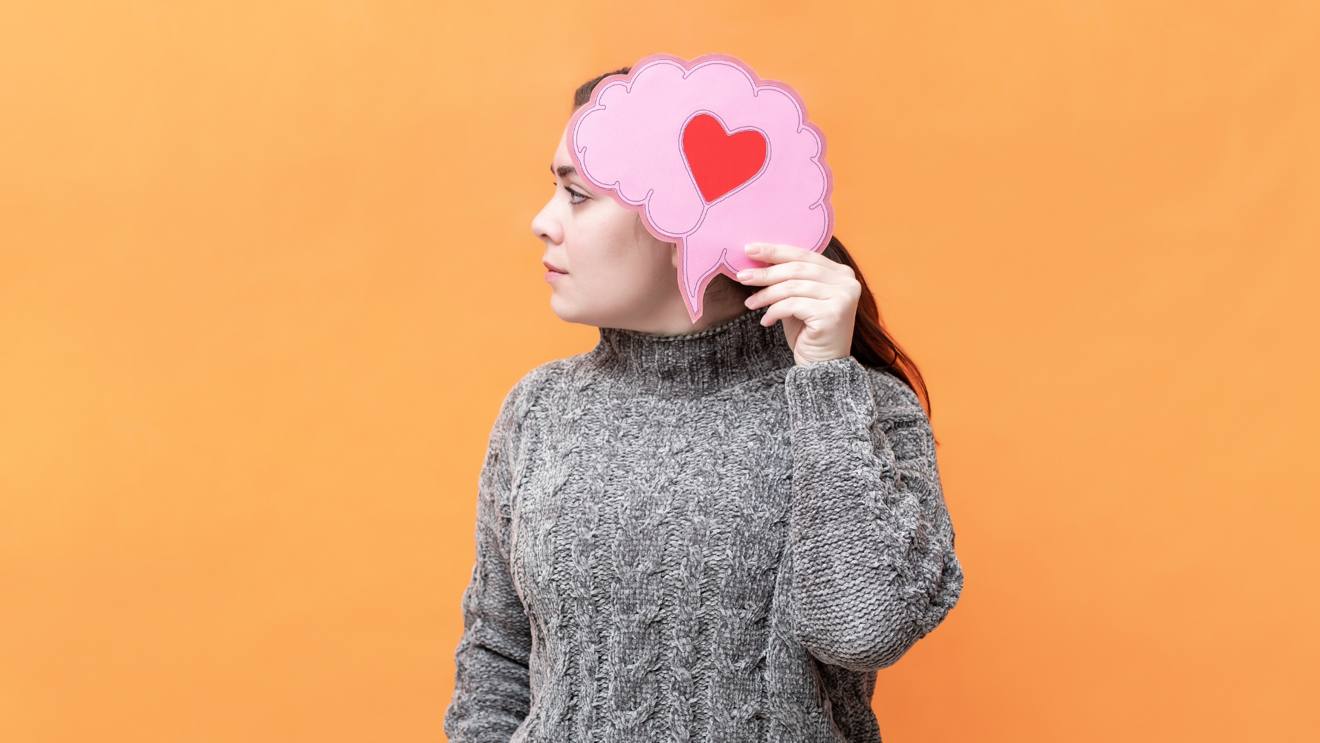 A woman holding paper cutout of brain with heart symbol on it denoting emotional intelligence.