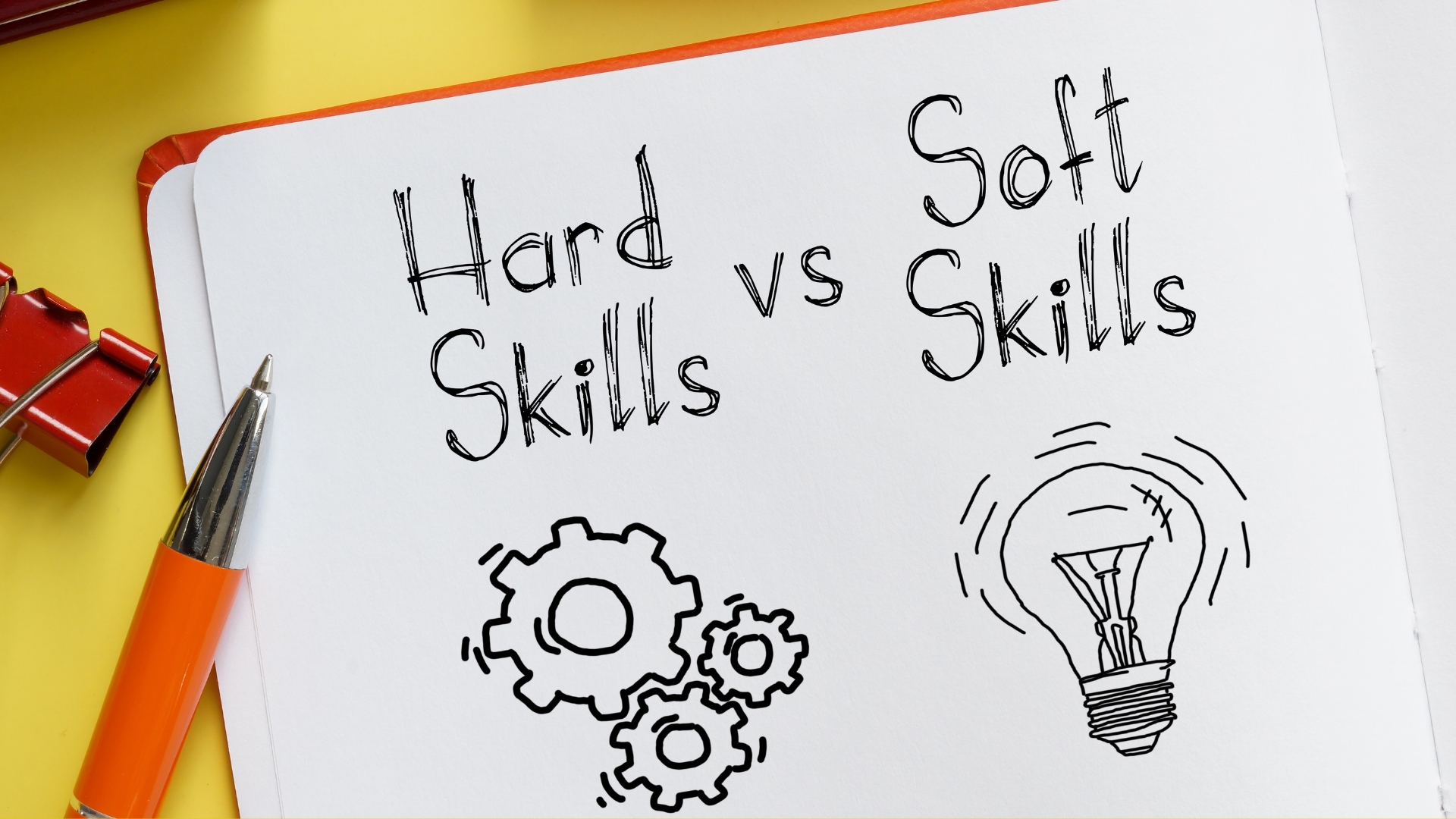 Notebook with 'Hard Skills vs Soft Skills' written, accompanied by a cog symbolizing hard skills and a light bulb symbolizing soft skills.